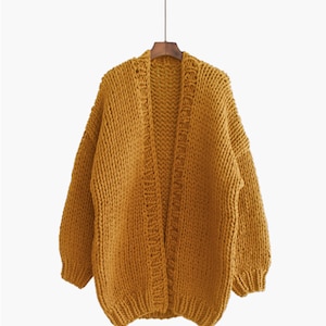 K&ouml;nnte beinhalten: Ein lang&auml;rmliger, senfgelber Cardigan mit grobmaschiger Strickstruktur. Der Cardigan hat einen V-Ausschnitt und eine lockere Passform.