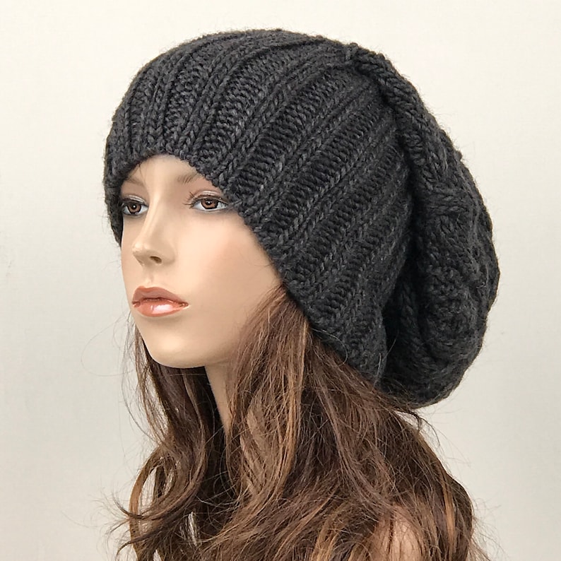 May include: A slouchy beanie hat in a dark gray color, knitted with a ribbed texture. The hat is made of soft yarn and has a relaxed fit.