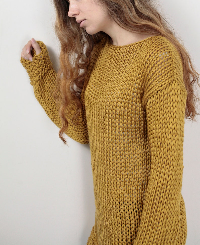May include: A mustard yellow knitted sweater with a loose fit and a round neckline. The sweater is made of a soft, chunky yarn and has a relaxed, casual style.