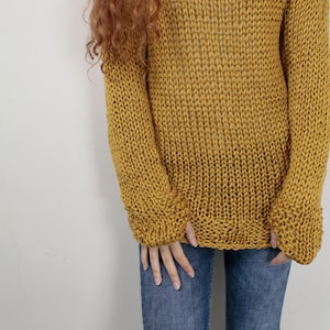 May include: A mustard yellow knitted sweater with a loose fit and long sleeves. The sweater is made of a chunky yarn and has a relaxed, casual style.