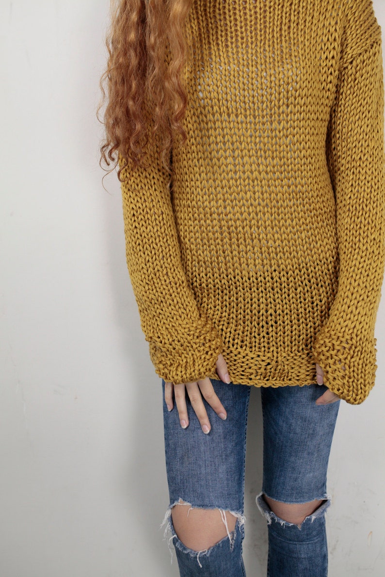 May include: A mustard yellow knitted sweater with a loose fit and long sleeves. The sweater is made of a chunky yarn and has a relaxed, casual style.