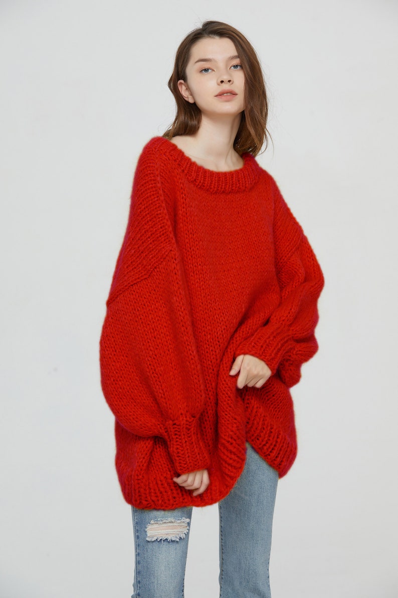K&ouml;nnte beinhalten: Ein roter Oversize-Strickpullover mit Rundhalsausschnitt und langen &Auml;rmeln. Der Pullover ist aus dickem Garn gefertigt und hat eine lockere Passform.