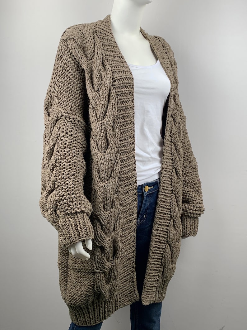 May include: A long, brown cable knit cardigan with a loose fit and oversized sleeves. The cardigan is made of a soft, chunky yarn and has a relaxed, casual style.