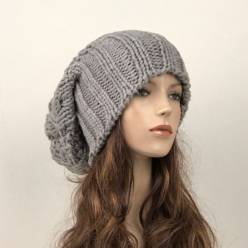 May include: A gray slouchy beanie hat made of knitted wool. The hat is worn by a mannequin with long brown hair.