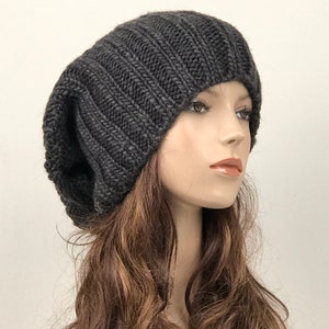 May include: A dark gray slouchy beanie hat made of knit fabric. The hat is soft and comfortable and has a relaxed fit.