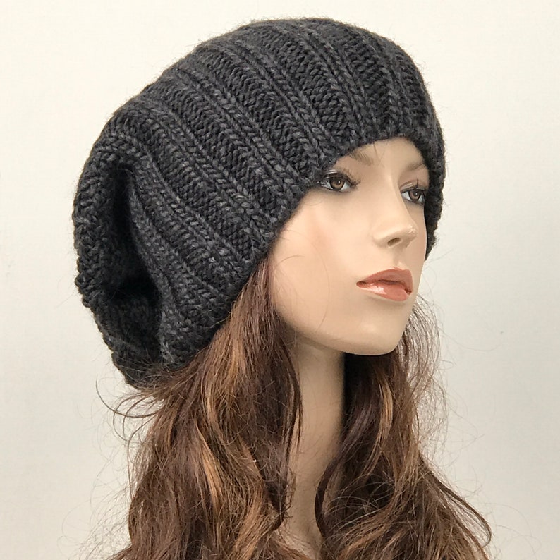 May include: A dark gray slouchy beanie hat made of knit fabric. The hat is soft and comfortable and has a relaxed fit.