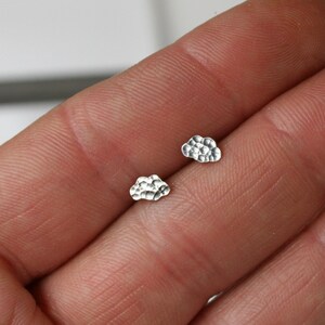May include: A pair of silver cloud-shaped stud earrings. The earrings are small and delicate, and they have a textured surface.