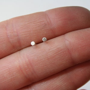 May include: A pair of small, silver stud earrings. The earrings are round and have a smooth, polished finish.
