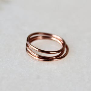 May include: Three thin rose gold rings stacked together. The rings are simple and delicate.