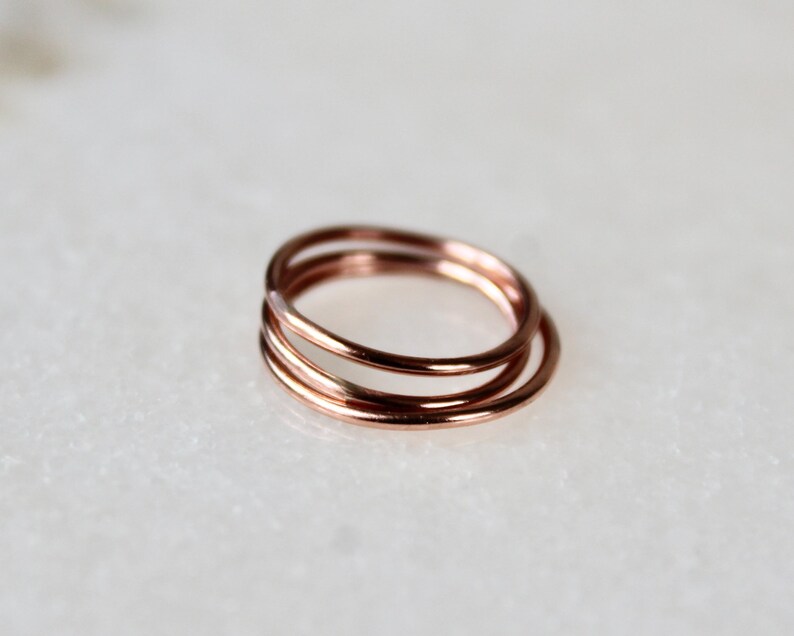 May include: Three thin rose gold rings stacked together. The rings are simple and delicate.