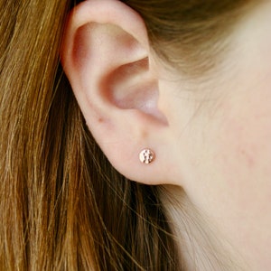 May include: A close-up of a person's ear with a small, round, hammered gold earring.