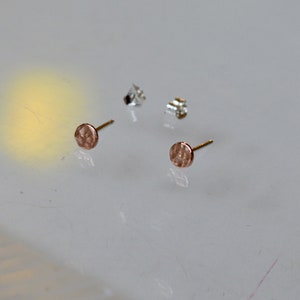 May include: A pair of small, round, hammered gold earrings with a textured surface.