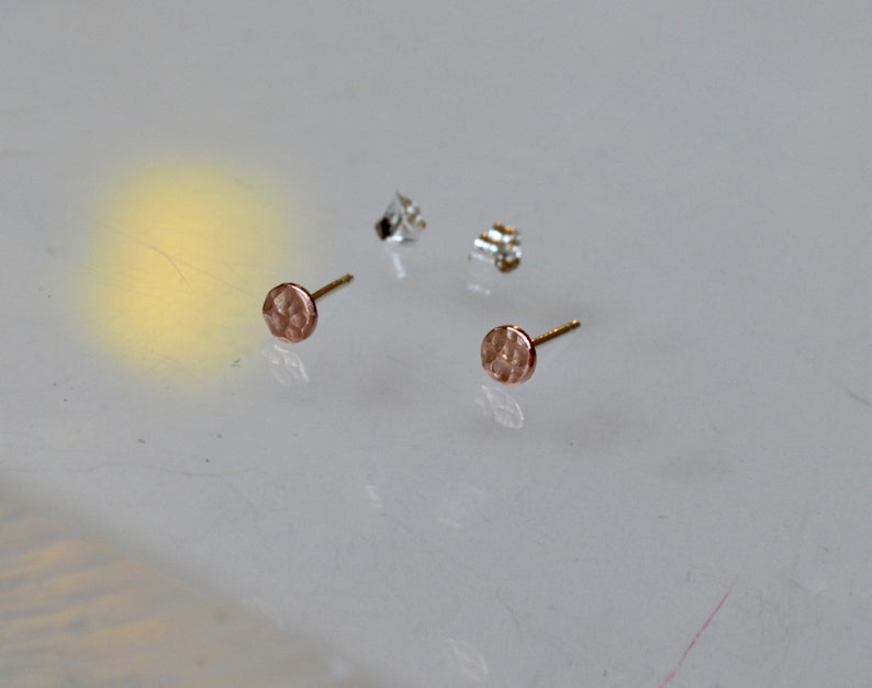May include: A pair of small, round, hammered gold earrings with a textured surface.