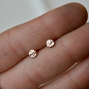 May include: A pair of small, round, hammered rose gold stud earrings.