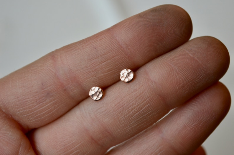May include: A pair of small, round, hammered rose gold stud earrings.