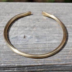 K&ouml;nnte beinhalten: Ein schlichtes goldenes Armreif-Armband aus glattem, abgerundetem Metall.