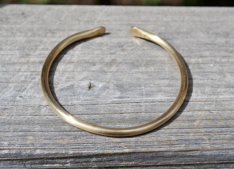 K&ouml;nnte beinhalten: Ein schlichtes goldenes Armreif-Armband aus glattem, abgerundetem Metall.
