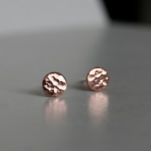 May include: A pair of small, round, hammered copper earrings. The earrings are a light copper color and have a textured surface.