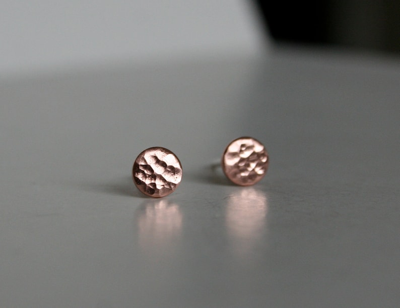 May include: A pair of small, round, hammered copper earrings. The earrings are a light copper color and have a textured surface.