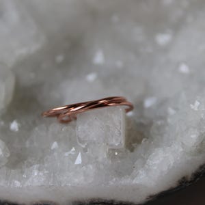 May include: A delicate, rose gold, triple-strand ring, resting on a white crystal surface.