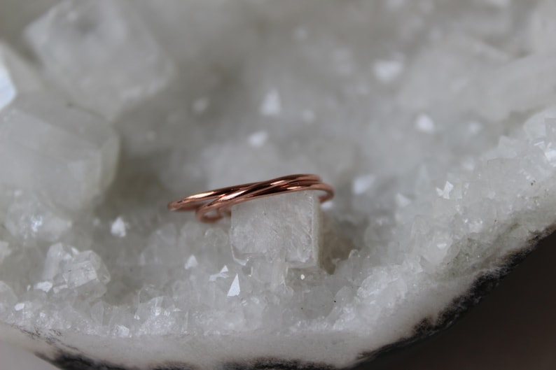 May include: A delicate, rose gold, triple-strand ring, resting on a white crystal surface.