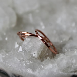May include: Two thin, hammered copper rings stacked on top of each other. The rings are a warm rose gold color and are sitting on a bed of white crystals.