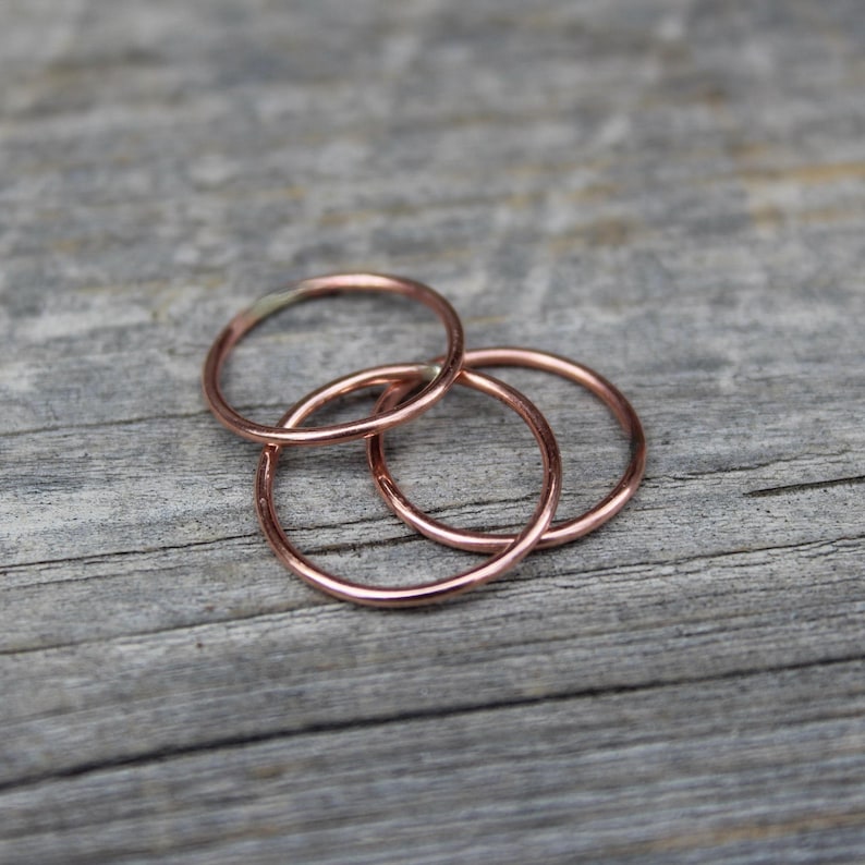 May include: Three simple copper rings stacked on top of each other on a wooden surface.