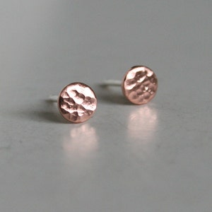 May include: A pair of small, round, hammered copper earrings. The earrings are a light rose gold color.