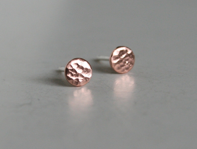 May include: A pair of small, round, hammered copper earrings. The earrings are a light rose gold color.