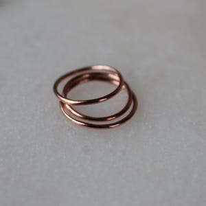May include: Three thin rose gold rings stacked on top of each other. The rings are simple and delicate.