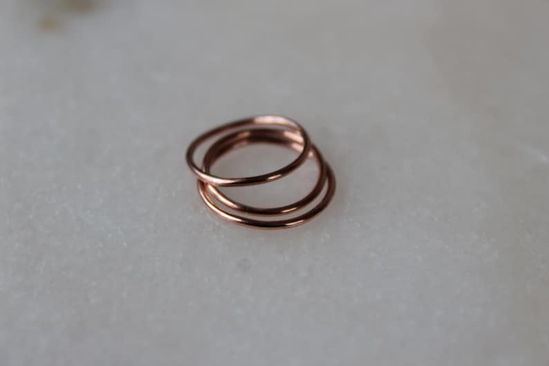 May include: Three thin rose gold rings stacked on top of each other. The rings are simple and delicate.