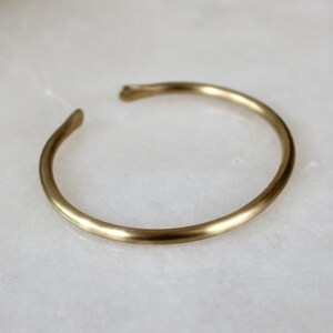 K&ouml;nnte beinhalten: Ein schlichtes, goldfarbenes Armreif-Armband aus glattem Metall.