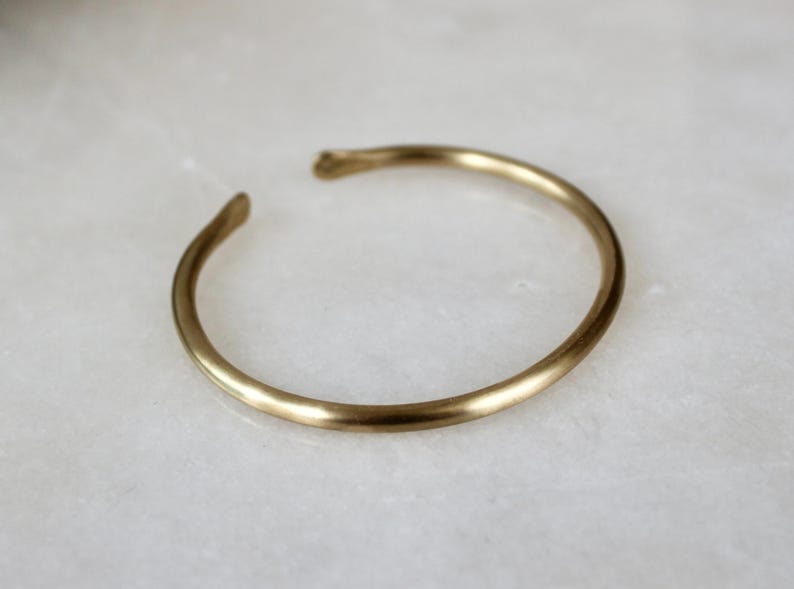 K&ouml;nnte beinhalten: Ein schlichtes, goldfarbenes Armreif-Armband aus glattem Metall.