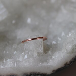 May include: A thin rose gold ring on a white crystal background.