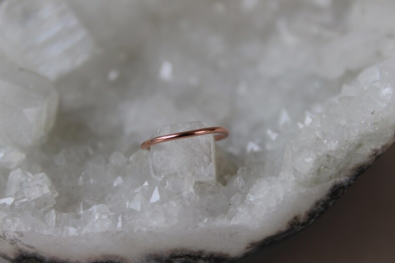 May include: A thin rose gold ring on a white crystal background.