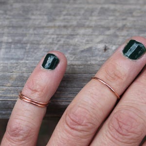 May include: Two thin rose gold rings on a finger. The ring on the index finger is a single band, while the ring on the middle finger is a double band.