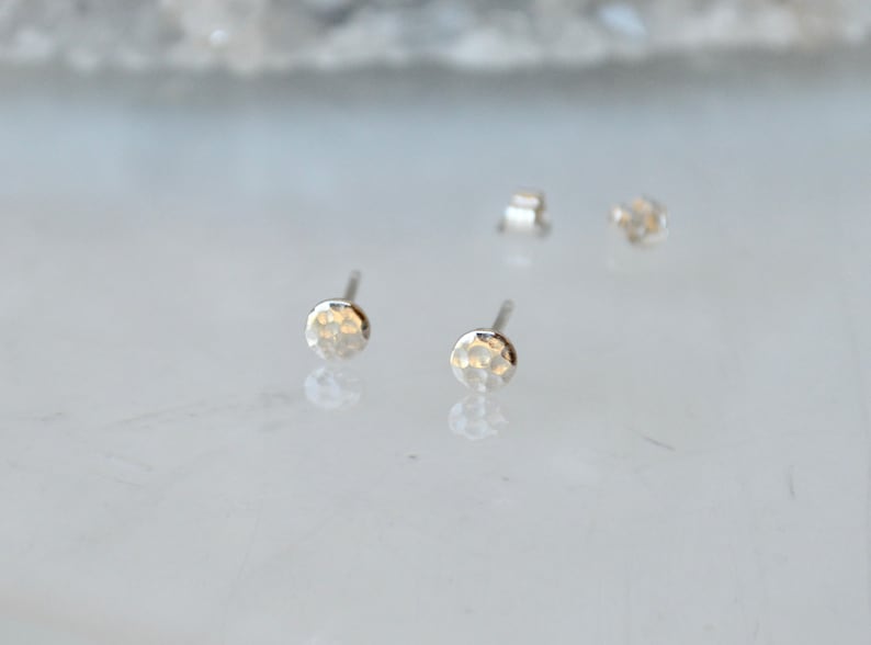 May include: A pair of silver hammered disc stud earrings. The earrings are small and delicate, with a hammered texture that gives them a unique look.