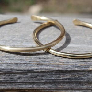 K&ouml;nnte beinhalten: Zwei goldfarbene Metallarmb&auml;nder, die &uuml;bereinander liegen. Die Armb&auml;nder sind schlicht und haben eine glatte, abgerundete Oberfl&auml;che.