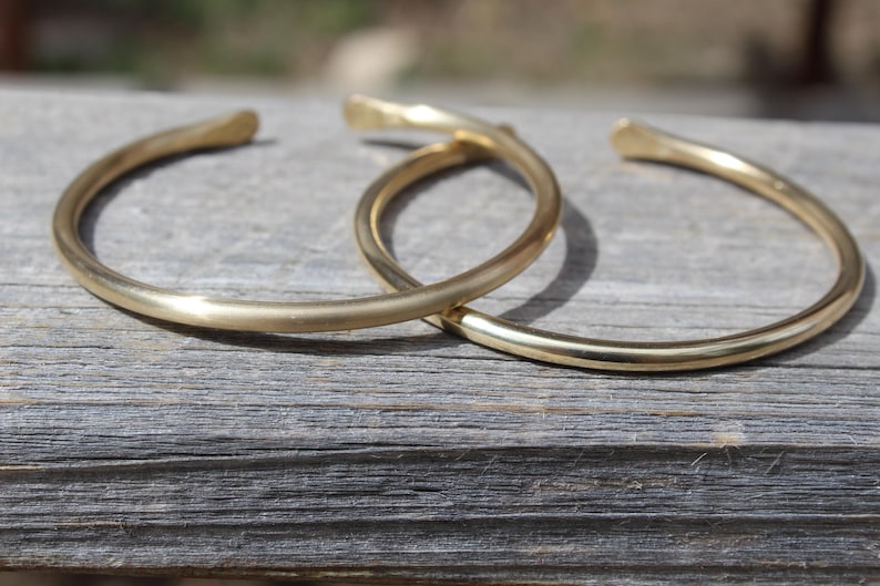 K&ouml;nnte beinhalten: Zwei goldfarbene Metallarmb&auml;nder, die &uuml;bereinander liegen. Die Armb&auml;nder sind schlicht und haben eine glatte, abgerundete Oberfl&auml;che.