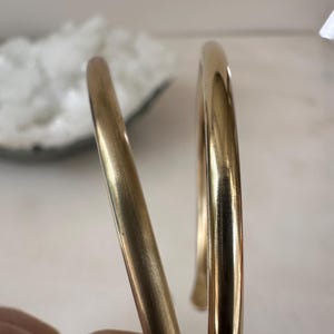K&ouml;nnte beinhalten: Zwei goldfarbene Metallarmb&auml;nder, eines etwas breiter als das andere, mit einer glatten, polierten Oberfl&auml;che.
