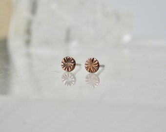 May include: A pair of small, round, copper-colored earrings with a textured, sunburst design.
