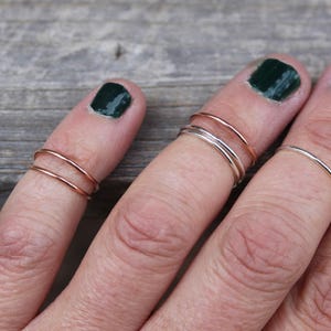 May include: A hand wearing multiple thin gold and silver rings on different fingers. The rings are stacked on top of each other.