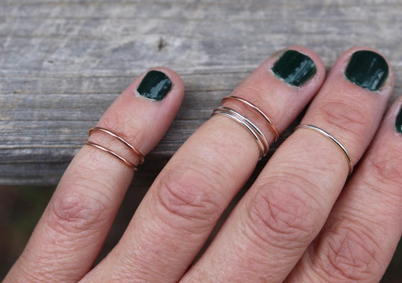 May include: A hand wearing multiple thin gold and silver rings on different fingers. The rings are stacked on top of each other.