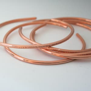 May include: Four copper bangles stacked on top of each other. The bangles are smooth and shiny.
