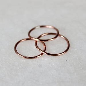 May include: Three thin rose gold rings stacked on top of each other. The rings are simple and delicate.