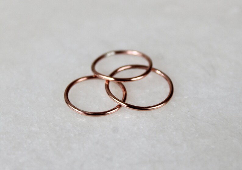 May include: Three thin rose gold rings stacked on top of each other. The rings are simple and delicate.