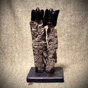 May include: Two black birds perched on top of two tree trunks, the trunks are attached to a black wooden base.