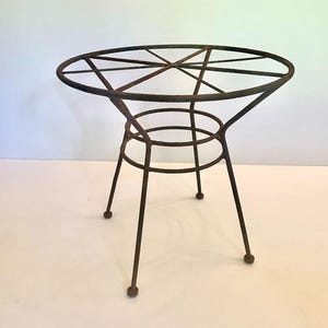 May include: A vintage, round, metal side table with a rusty brown finish. The tabletop features a geometric design, supported by a central ring and three angled legs. The table is approximately 24 inches in diameter and 20 inches tall.