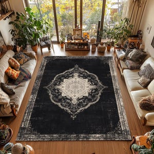May include: A large, rectangular black area rug with an ornate, distressed design. The rug features a central medallion in cream and a border with a similar pattern. The rug is placed on a hardwood floor in a living room setting.