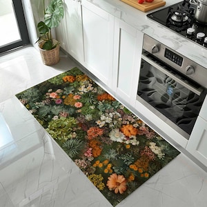 Puede incluir: Una alfombra de cocina rectangular con un diseño floral detallado. La alfombra muestra una densa disposición de flores en tonos naranja, blanco, rosa y amarillo, sobre un fondo de follaje verde. La alfombra está colocada frente a una encimera de cocina.